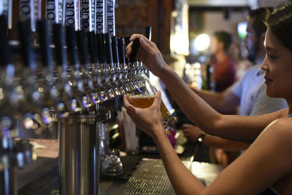 Female bartender pours craft beer in a lively pub setting, creating an inviting atmosphere.