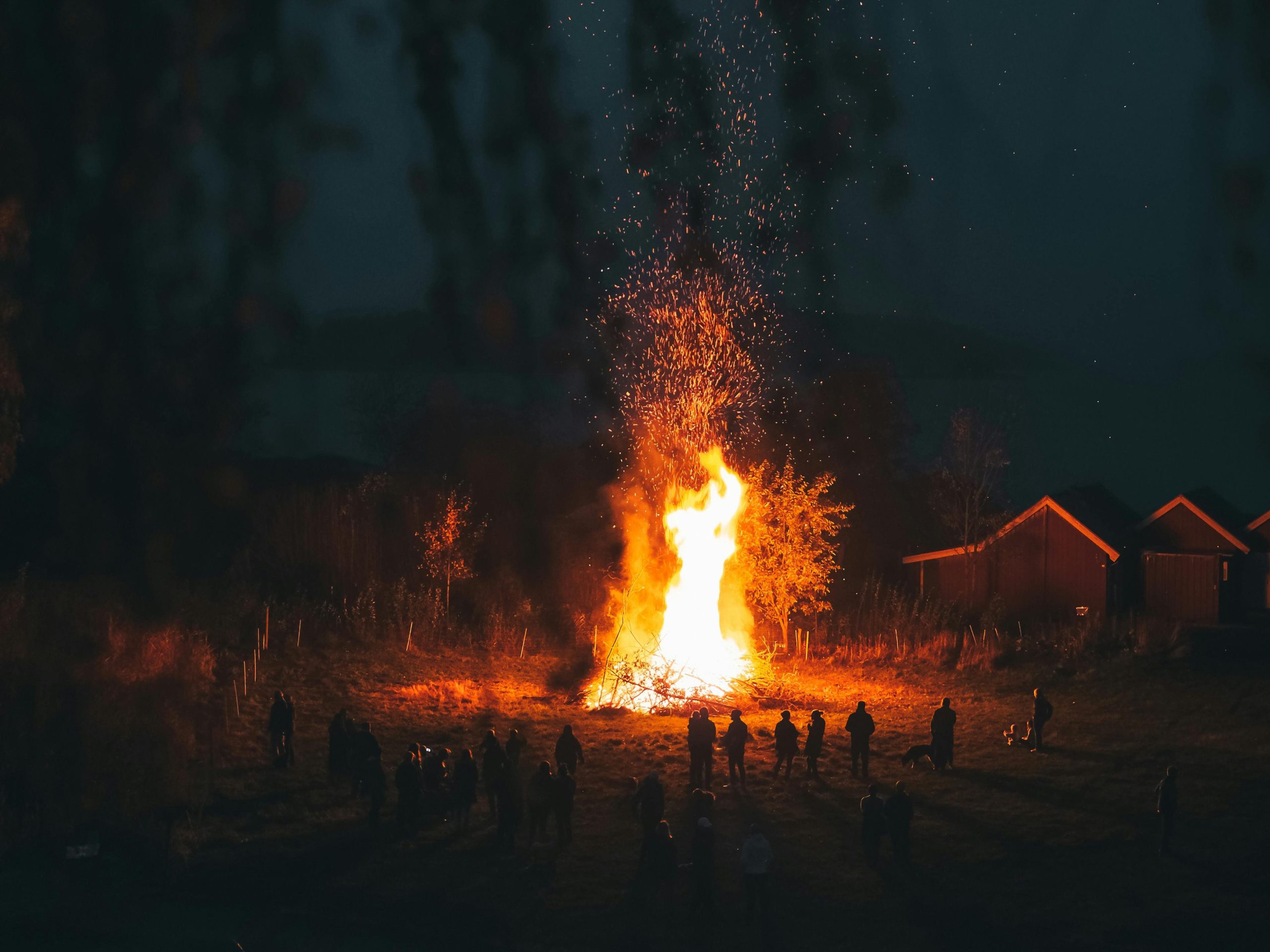 Large bonfire with people silhouetted against the night sky, creating a warm, communal atmosphere.